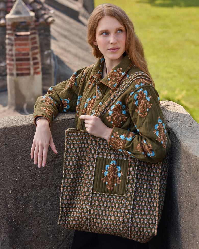 Model holding the deep olive Traveler Tote, showing its floral print, long handles, and large front pocket.