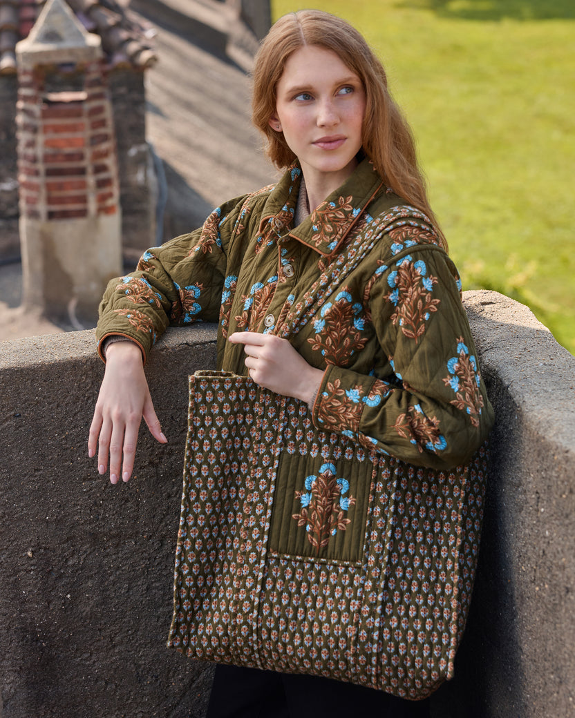 Model holding the deep olive Traveler Tote, showing its floral print, long handles, and large front pocket.
