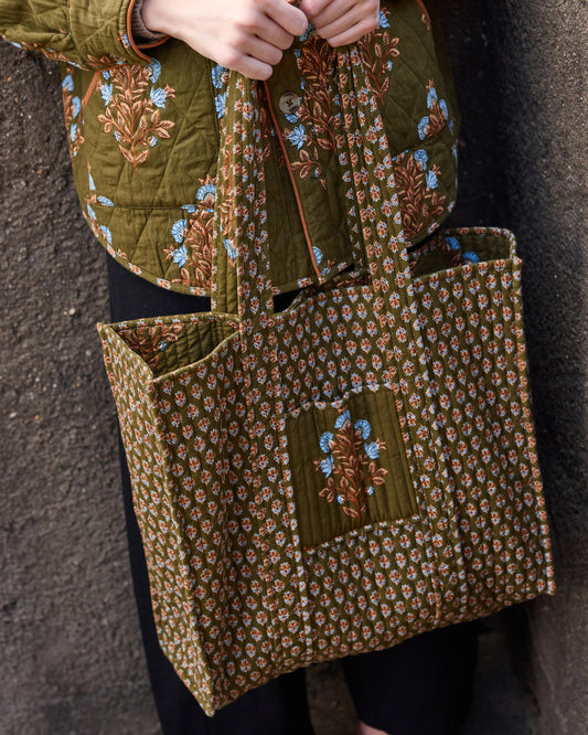 Close-up of the deep olive Traveler Tote showing its quilted floral panels, contrasting patterned front pocket, and handles.