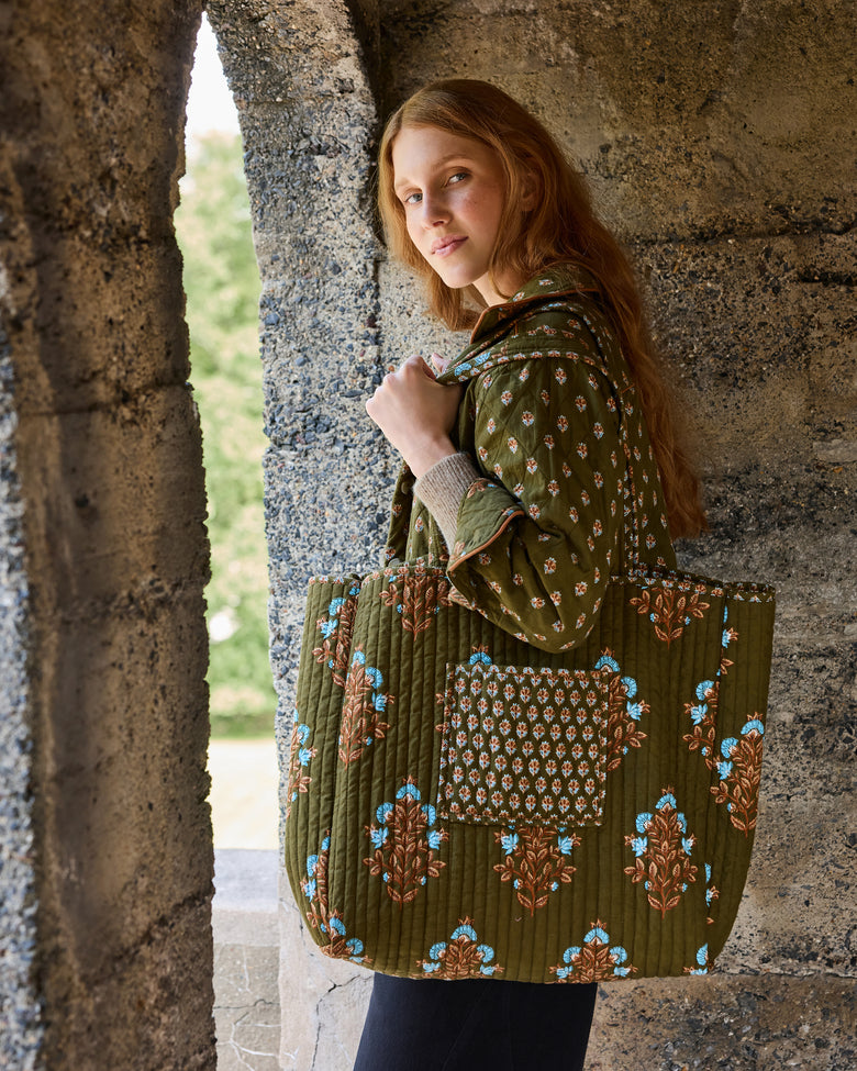 Side view of the deep olive Traveler Tote being carried, showing its large size, long handles, floral print, and front pocket.