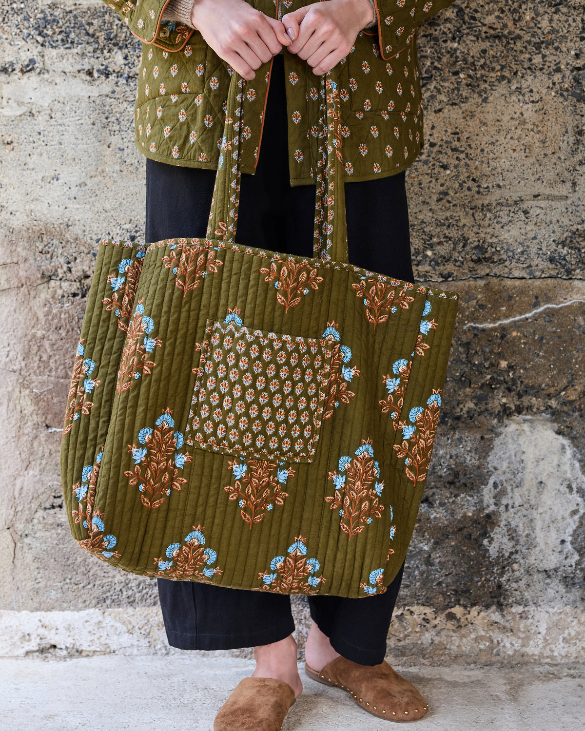 Front view of the deep olive Traveler Tote showing its quilted floral design, contrasting patterned pocket, and long handles.