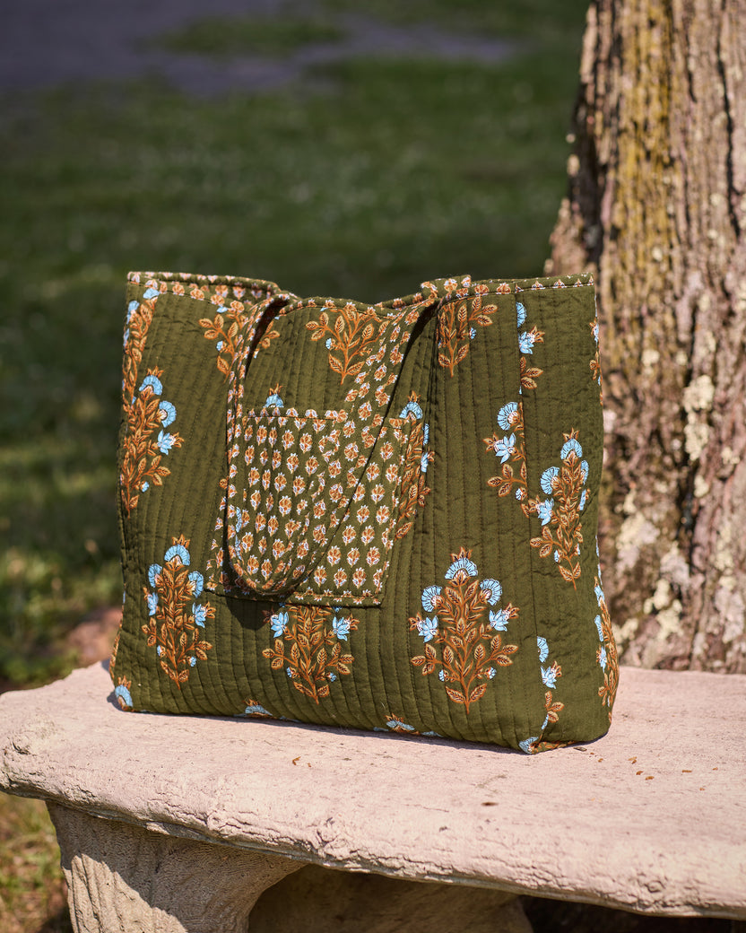 Deep olive floral-print quilted tote bag shown upright on a stone bench.