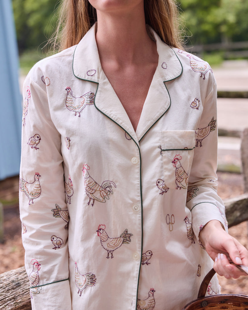 Close view of the buff Embroidered Hens pajama top with a notched collar, green piping, chest pocket, buttons, and chicken illustrations.