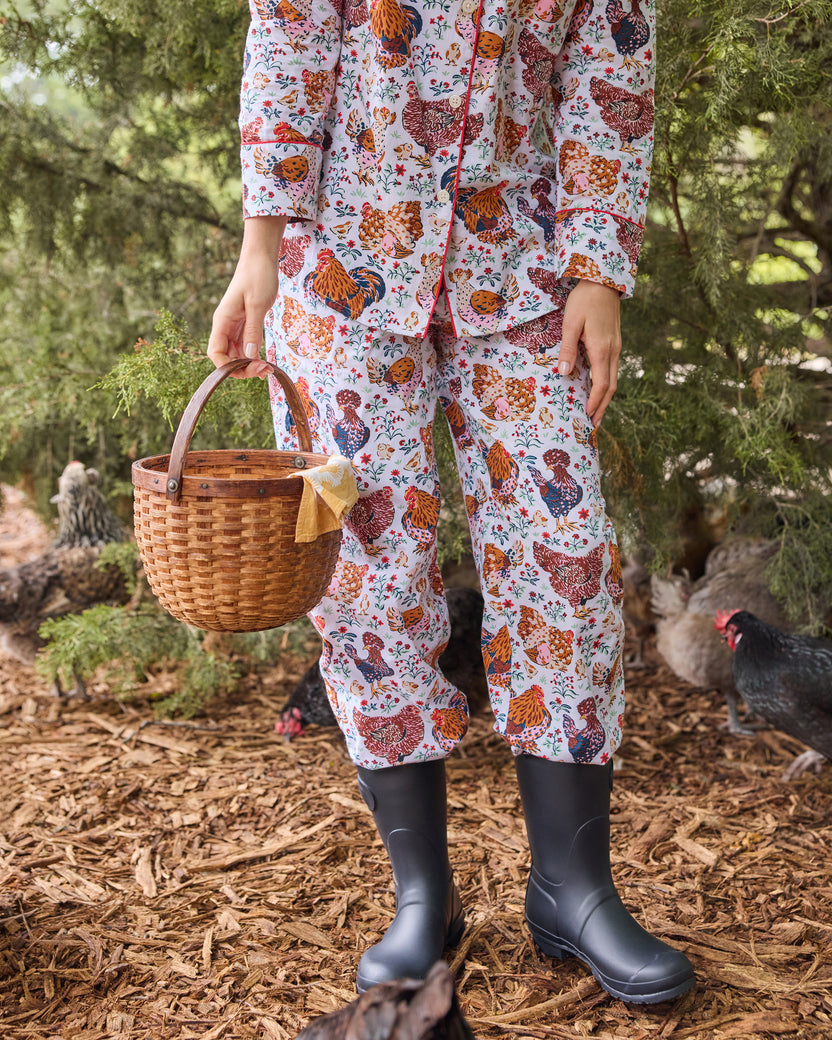 Close-up of the floral chicken-print pajama pants worn with tall boots beside a wicker basket.