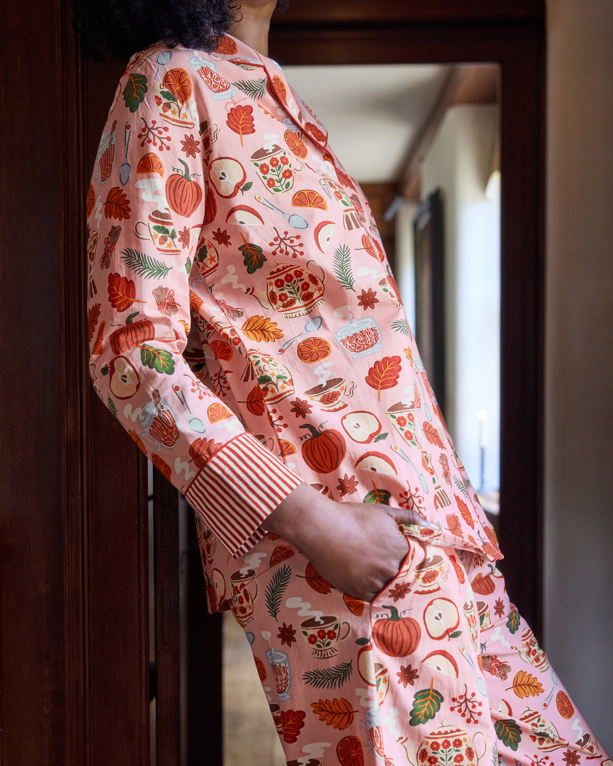Side view of the pink Autumn Cafe long pajama set, showing the buttoned top, striped cuff, matching pants, and allover tea, fruit, leaf, and biscuit-jar print.