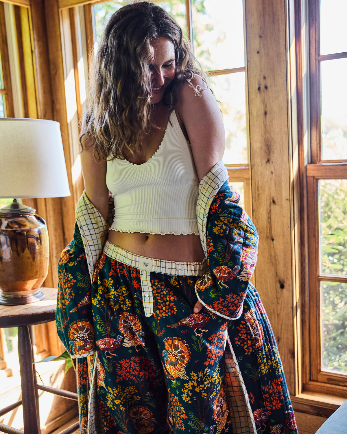Person wearing navy Turkey Trot pajama pants with turkey and autumn foliage print, with a matching robe draped around the arms.