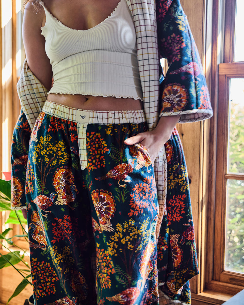 Close-up of navy Turkey Trot pajama pants showing the contrasting plaid waistband, button fly, side pocket, and turkey print.