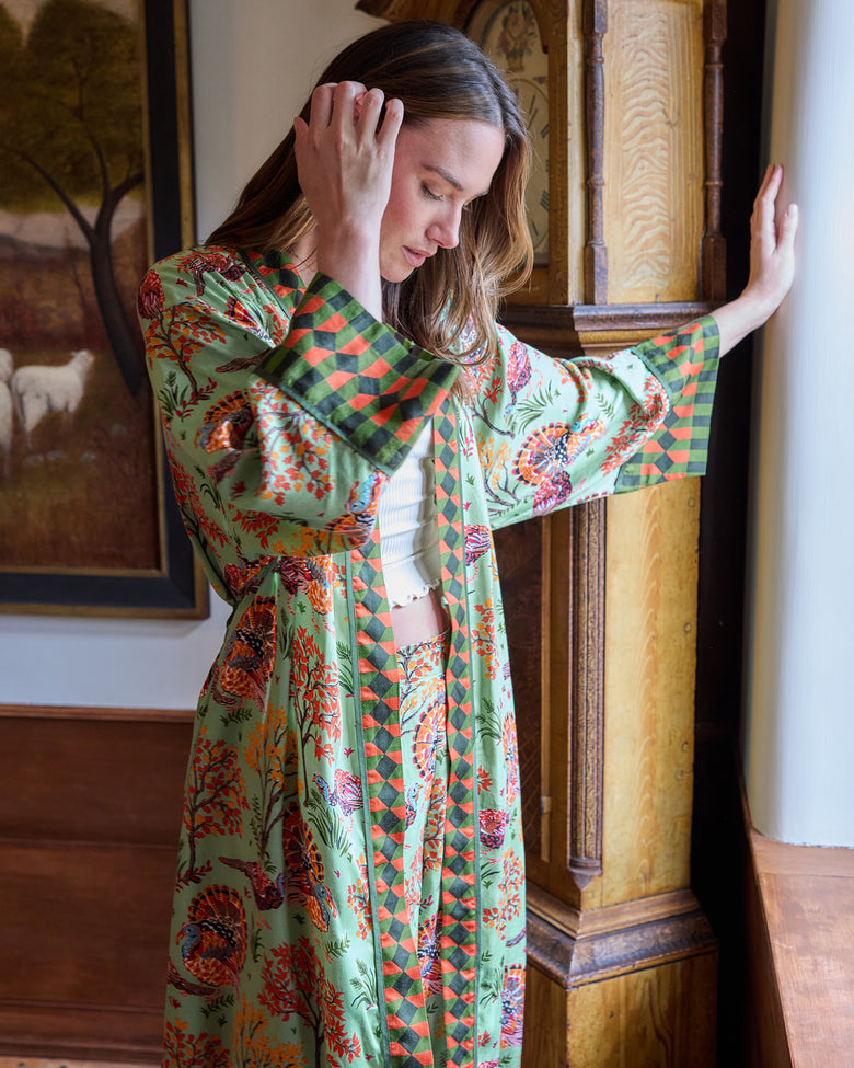 Side view of a person wearing a soft sage Turkey Trot long robe with turkey and autumn foliage print and contrasting geometric trim.
