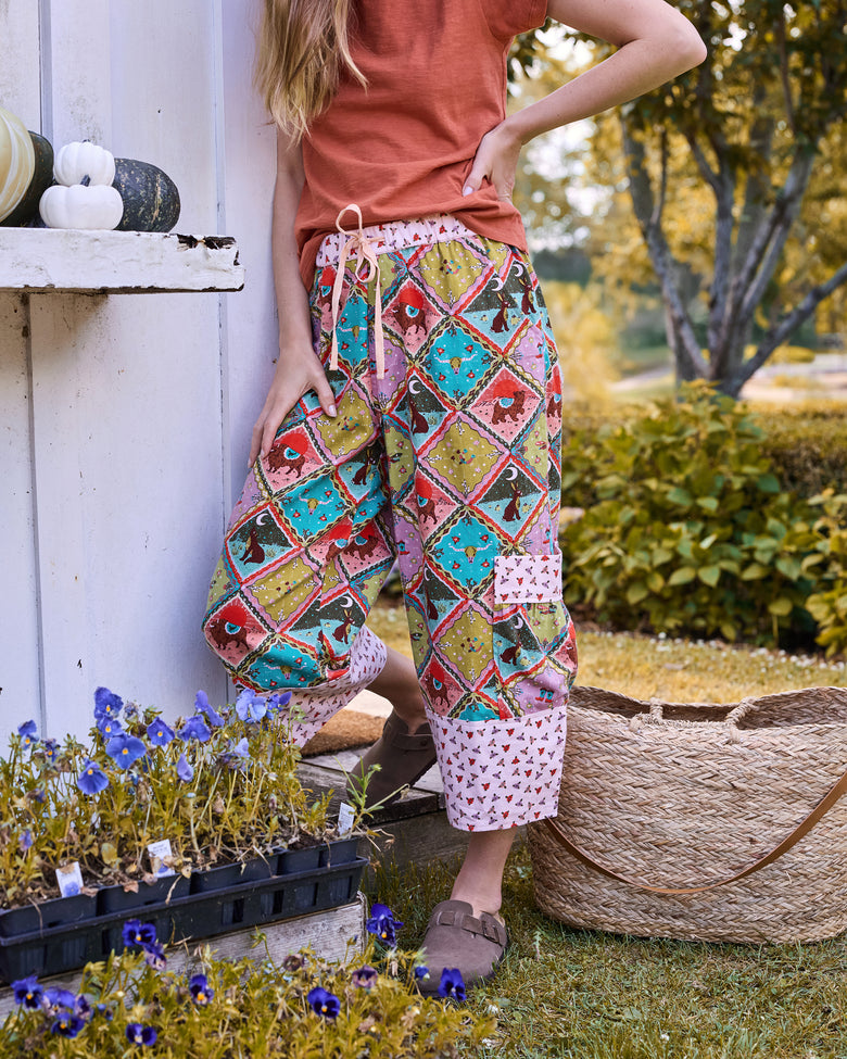 Person wearing cropped printed pants with a drawstring waist, large side pockets, and contrasting patterned cuffs outdoors.
