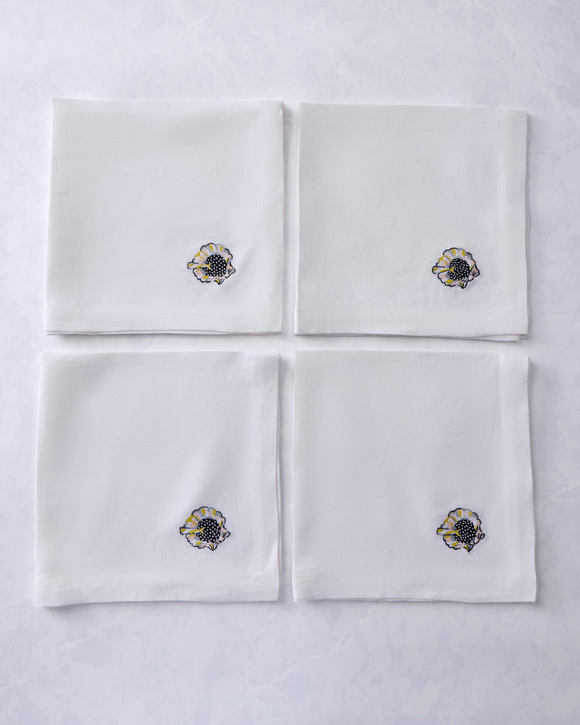 Four white dinner napkins arranged in a square, each embroidered with a shell motif.