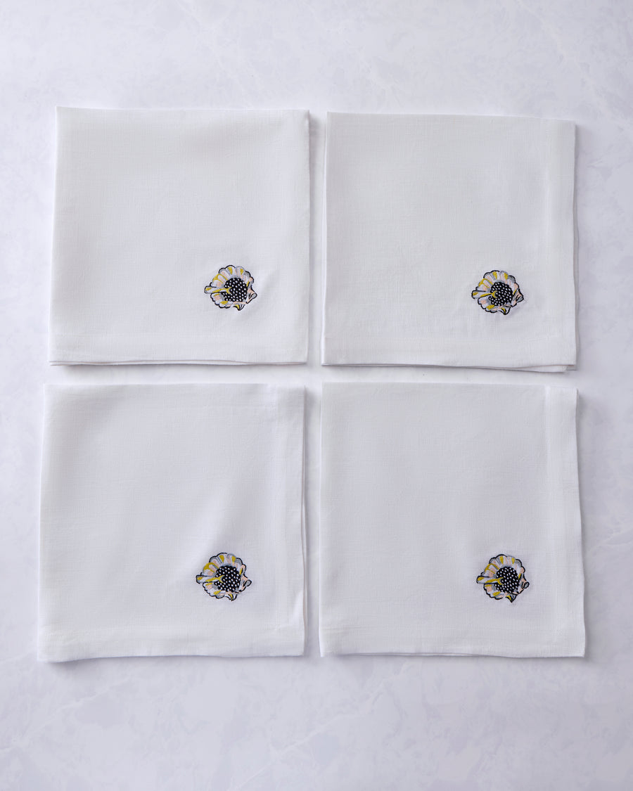 Four white dinner napkins arranged in a square, each embroidered with a shell motif.