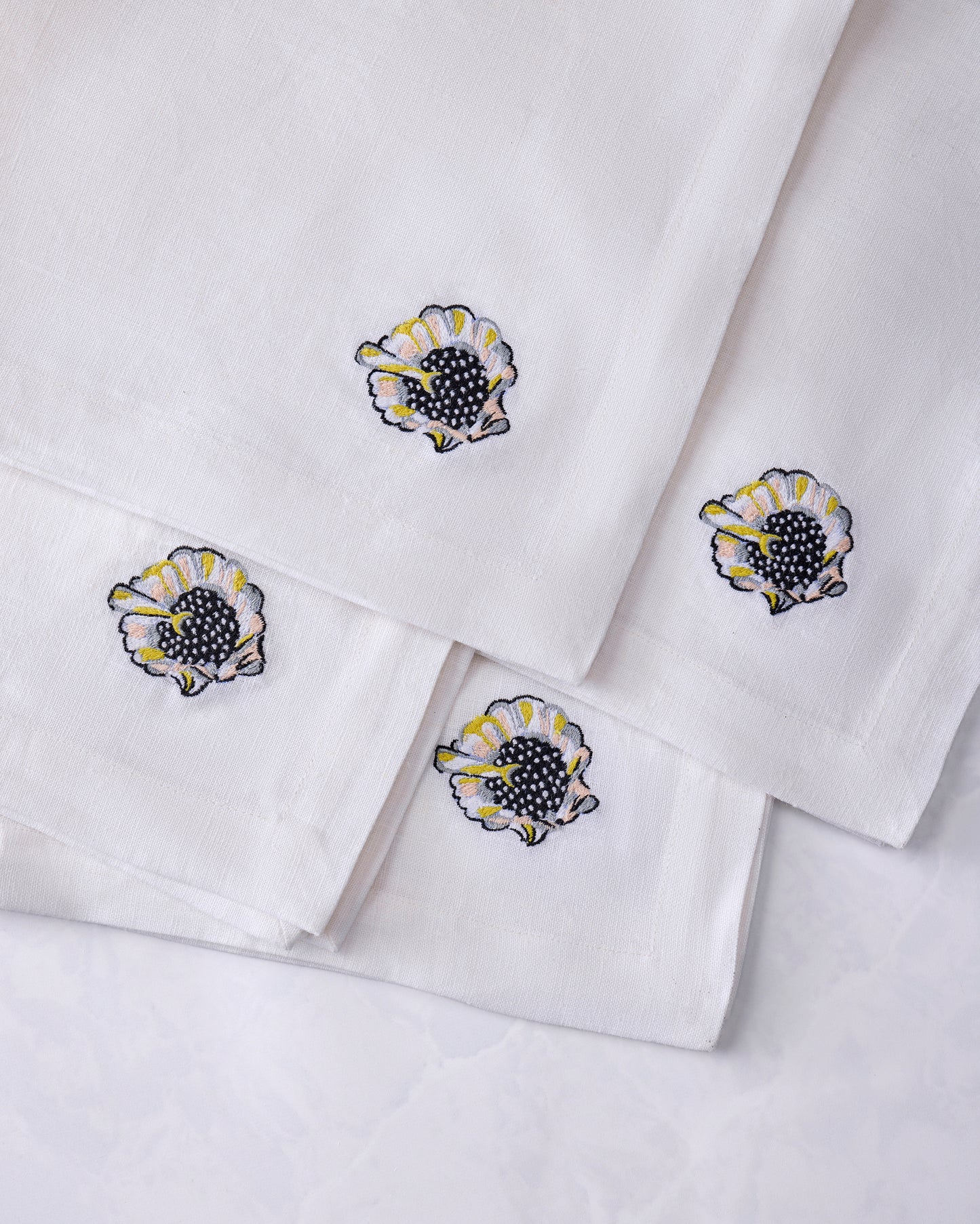 Four overlapping white dinner napkins with embroidered shell motifs.