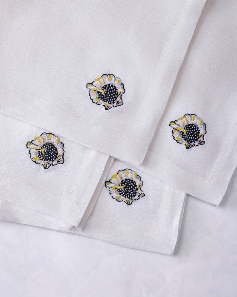 Four overlapping white dinner napkins with embroidered shell motifs.