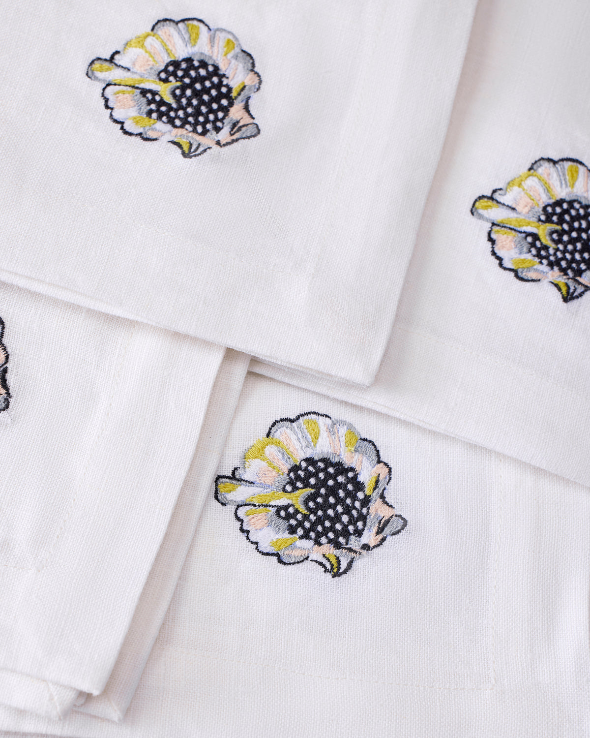 Close-up of embroidered shell motifs on overlapping white dinner napkins.