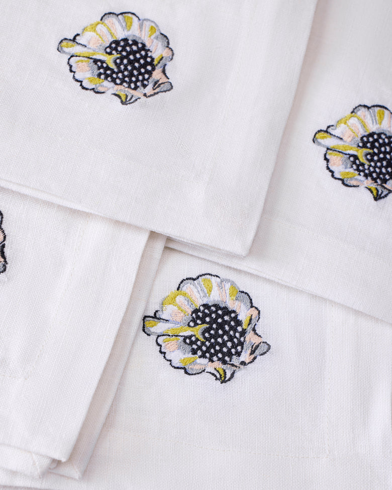 Close-up of embroidered shell motifs on overlapping white dinner napkins.