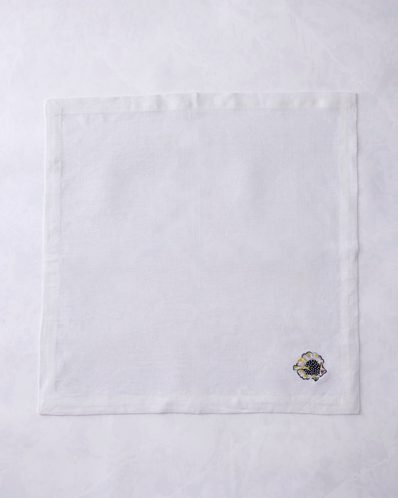 Single white dinner napkin shown flat with an embroidered shell motif near the lower-right corner.