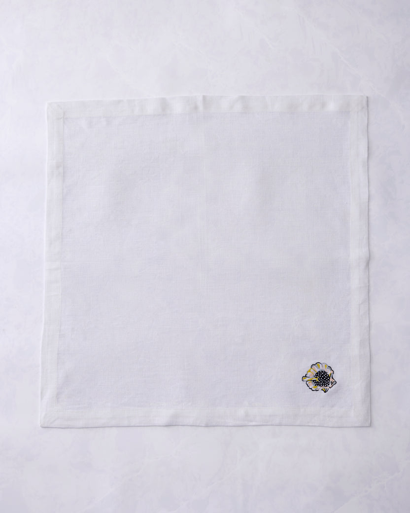 Single white dinner napkin shown flat with an embroidered shell motif near the lower-right corner.