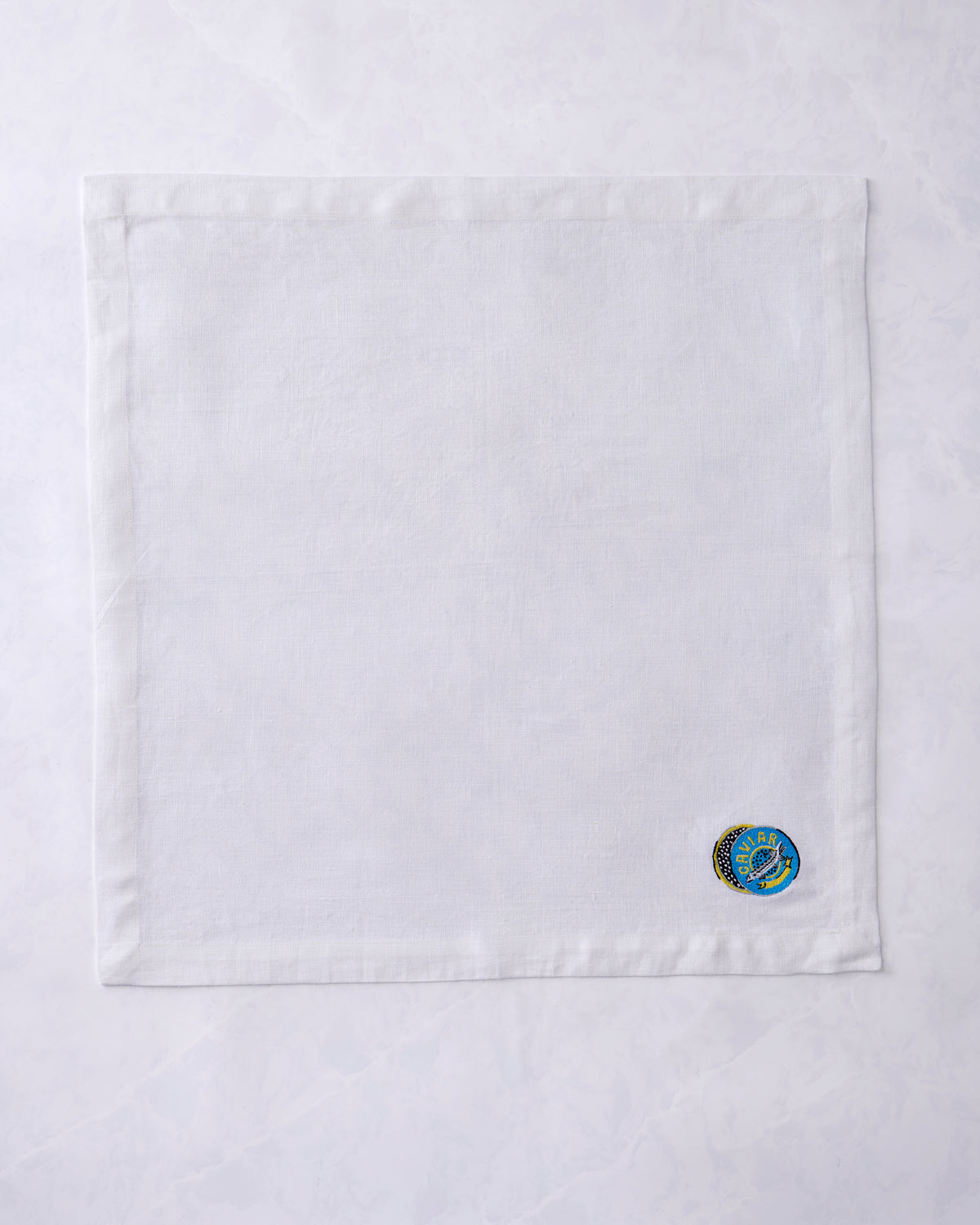 Single unfolded dinner napkin with a small embroidered caviar design near one corner.