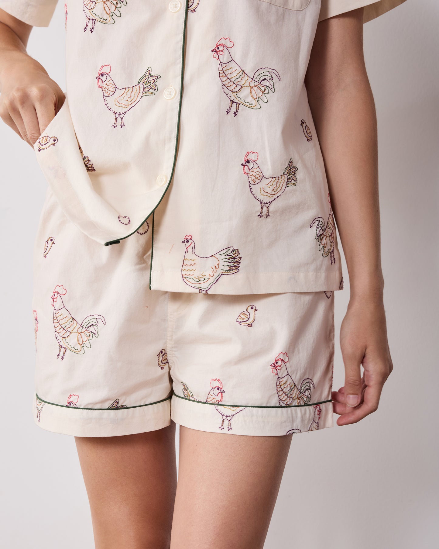 Close detail of the short pajama set showing embroidered hens, button front, chest pocket, and piped shorts hem.