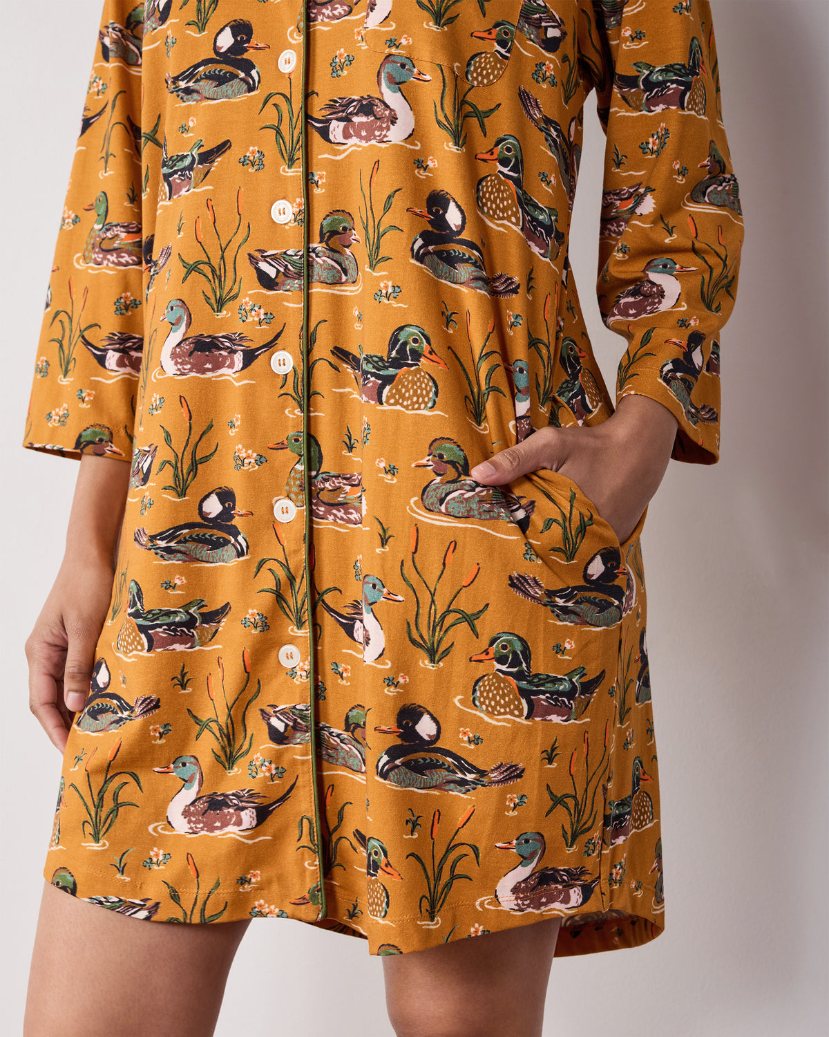 Close view of the mustard Duck Pond sleep shirt showing its button front, three-quarter sleeves, pockets, and duck-and-reed print.