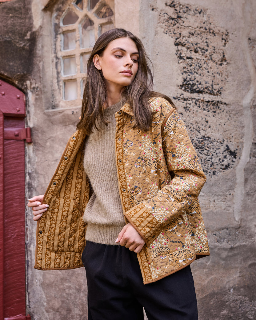 Model wearing the mustard quilted jacket open to show its contrasting botanical print lining.
