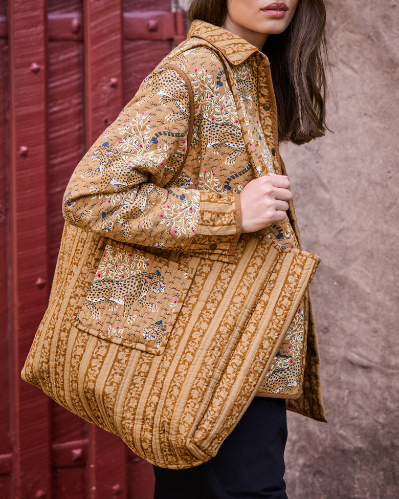 Traveler tote carried over one shoulder, featuring a tan striped quilted design with leopard and botanical panels.