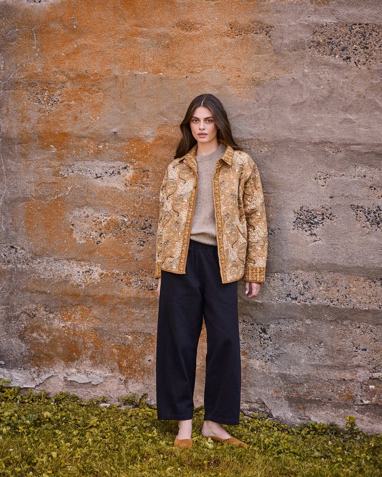 Front view of a patterned quilted jacket worn with a sweater and black wide-leg trousers.