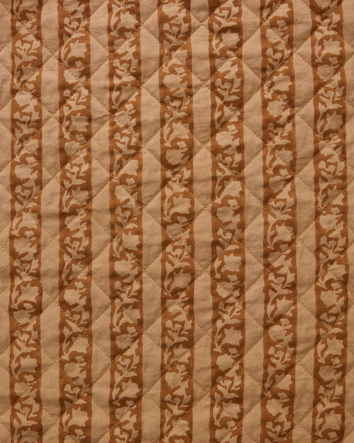 Mustard Seed fabric swatch with alternating tan stripes and floral vine patterns on a quilted surface.
