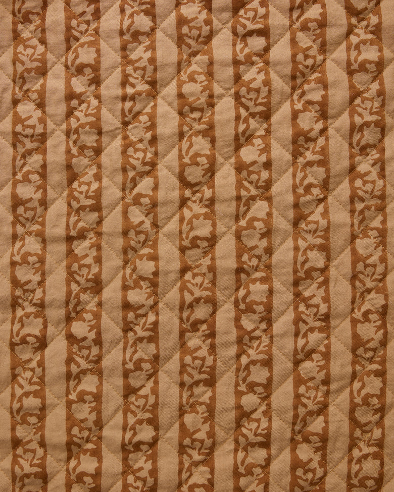 Close-up of quilted tan fabric with alternating vertical stripes and floral motifs.