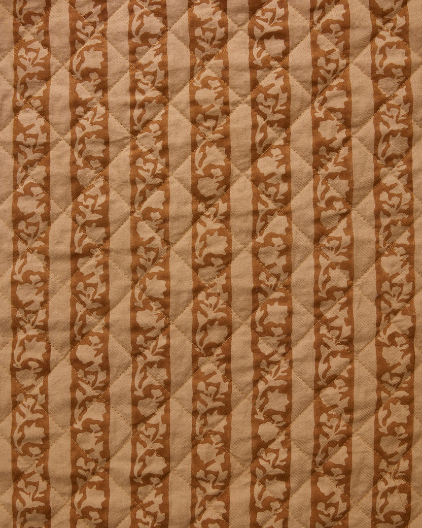 Close-up of quilted tan fabric with alternating vertical stripes and floral motifs.