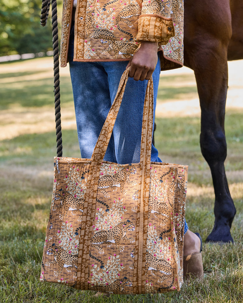 Front view of a quilted tote bag with a spotted big-cat and floral print, held beside a horse.