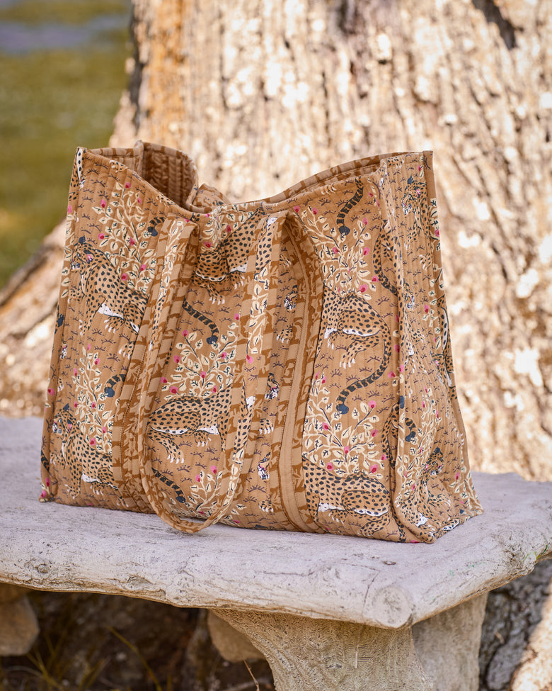 Quilted tote bag with a spotted big-cat and floral print displayed on a stone bench.