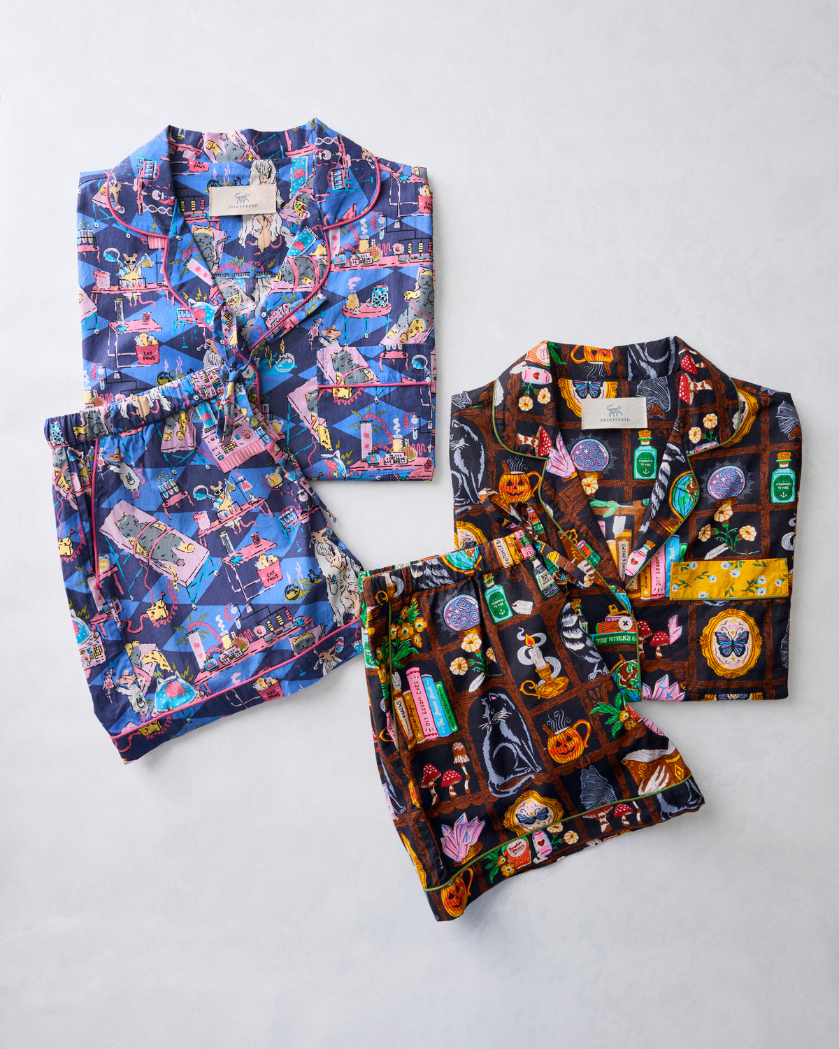Two short pajama sets from the Halloween Best bundle, one in a blue-purple Enchanted Study print and one in a dark It's Alive print, arranged flat.