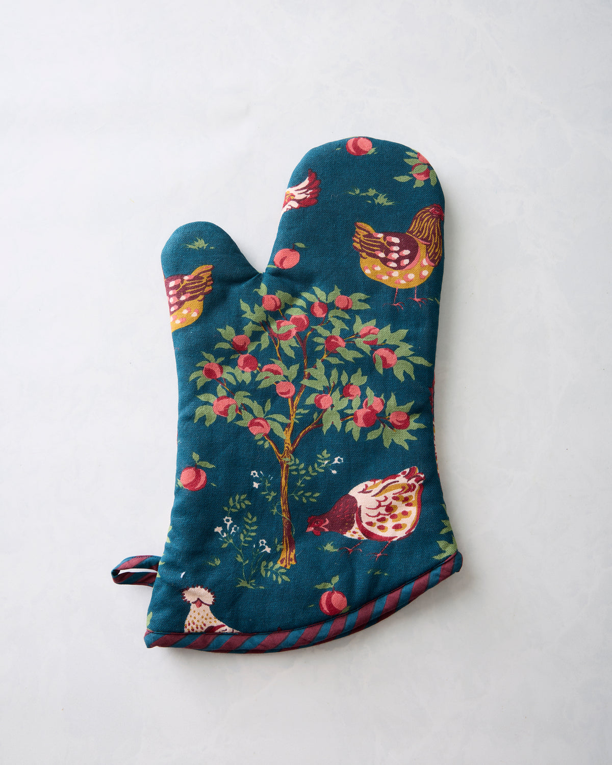 Oven mitt showing the dark teal chicken-and-apple-tree print, striped trim, and hanging loop from the opposite side.