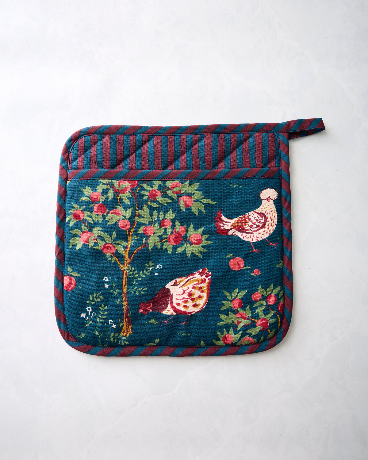 Front of a navy Hen House pot holder with a chicken-and-apple tree print and striped edging.