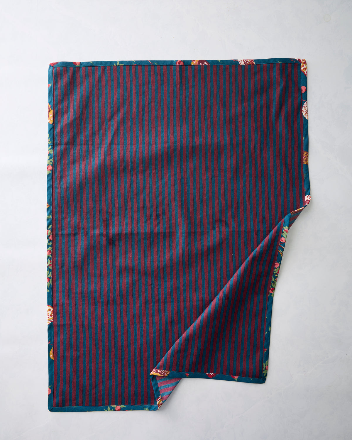 Tea towel showing its reverse side with dark teal and burgundy vertical stripes; a corner is folded to reveal the printed edge.