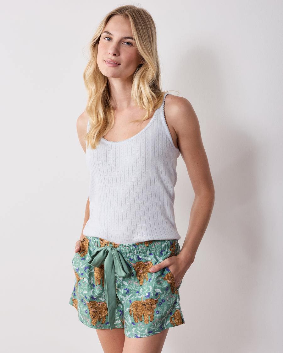 Front three-quarter view of green Highland cow-print pajama shorts with pockets and a satin tie
