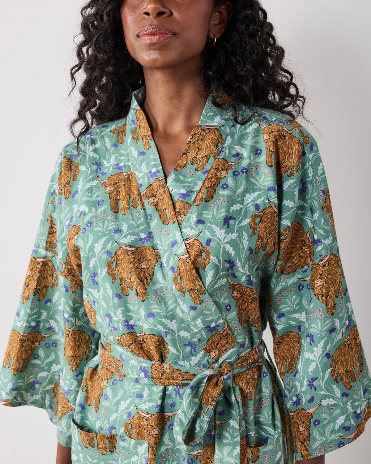 Close-up of the green Highland Cows robe showing the wrap-style neckline, wide sleeve, tied belt, and cow print.