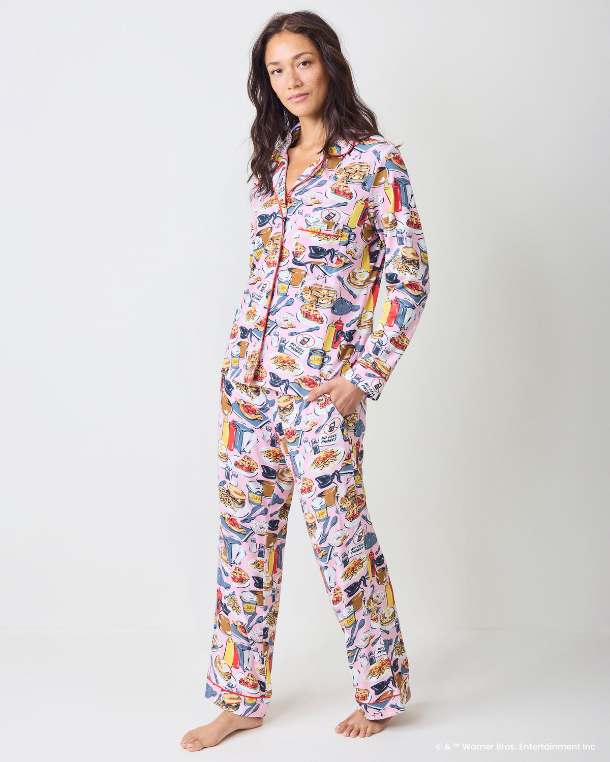 Person wearing a pink long-sleeve pajama set with a button-front top and straight-leg pants covered in diner and food illustrations.