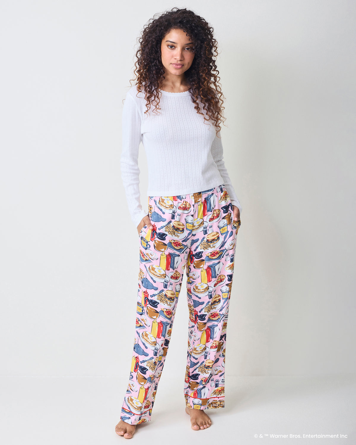 Front view of pink printed pajama pants with pockets, worn with a white ribbed sweater.