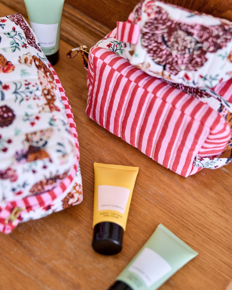 Close view of the Three’s Best Pouch set showing a chicken-print pouch, a red-and-white striped pouch, and three toiletry tubes on a wooden surface.