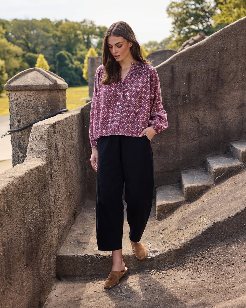 Full view of a person wearing a patterned button-front blouse with black wide-leg trousers and slip-on shoes.
