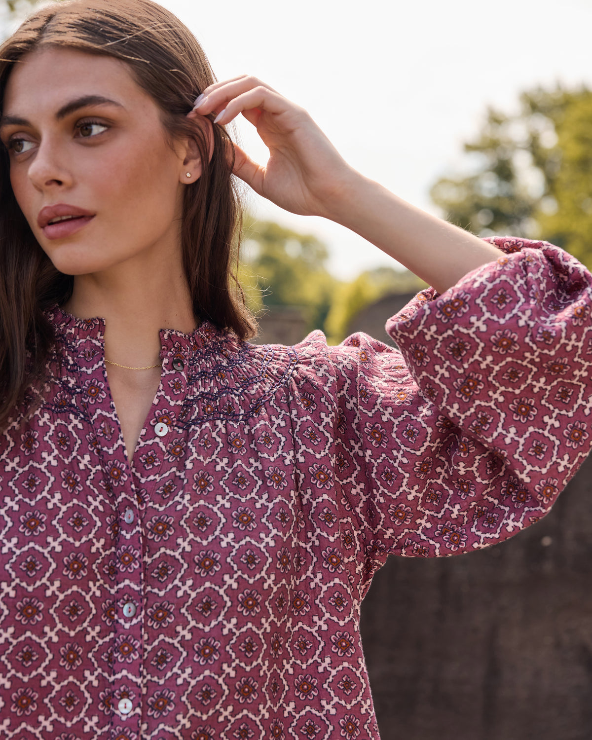 Close-up of a patterned blouse showing its gathered neckline, buttons, and long sleeve.