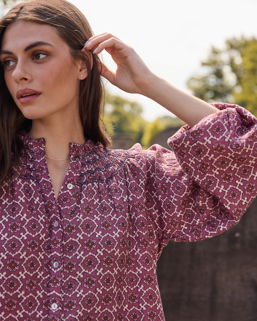 Close-up of a patterned blouse showing its gathered neckline, buttons, and long sleeve.