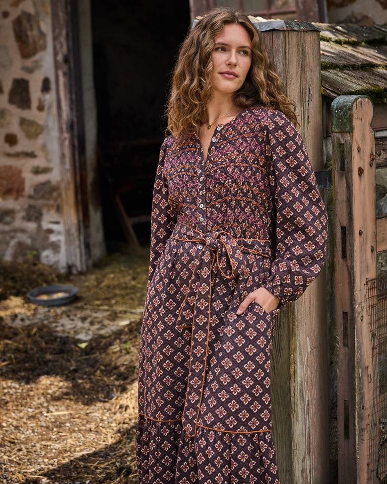 Close view of the Desert Primrose Shay Dress showing its patterned bodice, button-front neckline, long sleeves, waist tie, and pockets.