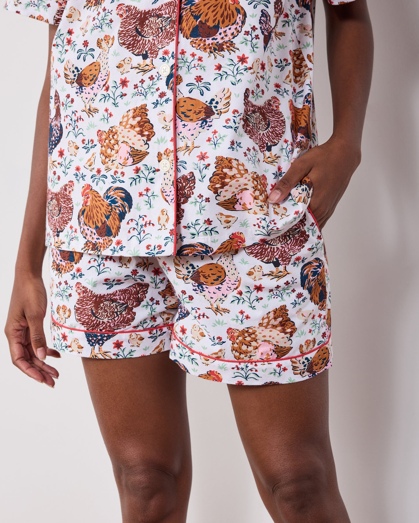 Close-up of a chicken-print short pajama set showing the button-front top, piping, and shorts pockets.
