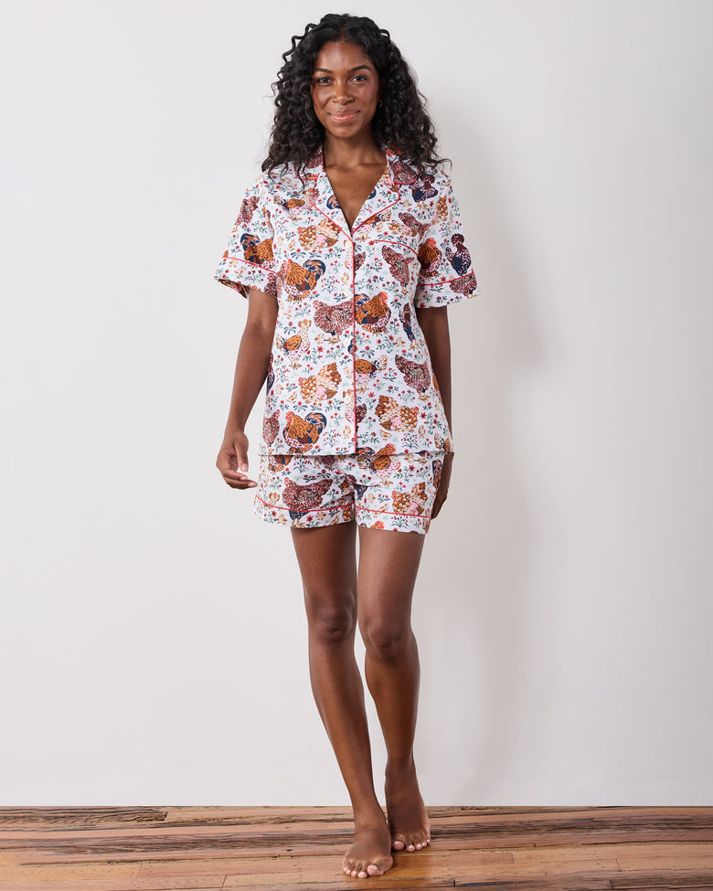 Model standing and wearing a short-sleeve pajama top with matching shorts in a chicken-and-floral print.