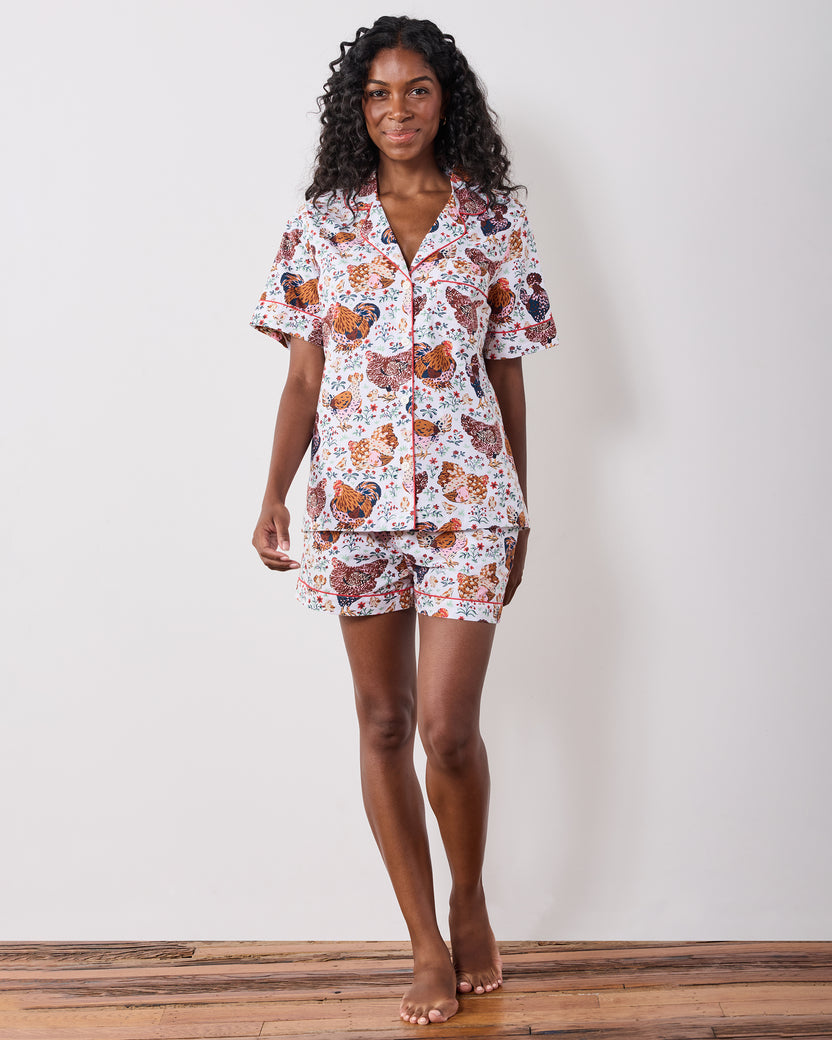Model standing and wearing a short-sleeve pajama top with matching shorts in a chicken-and-floral print.
