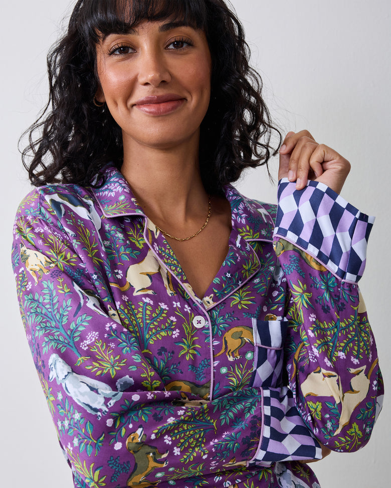 Close view of a purple dog-print pajama shirt showing the collar, buttons, pocket, and checkerboard cuff.