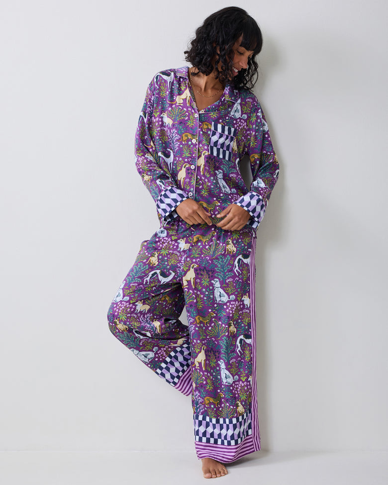 Model wearing a purple dog-print pajama set while lifting one leg to show the wide-leg pants and contrasting cuffs.